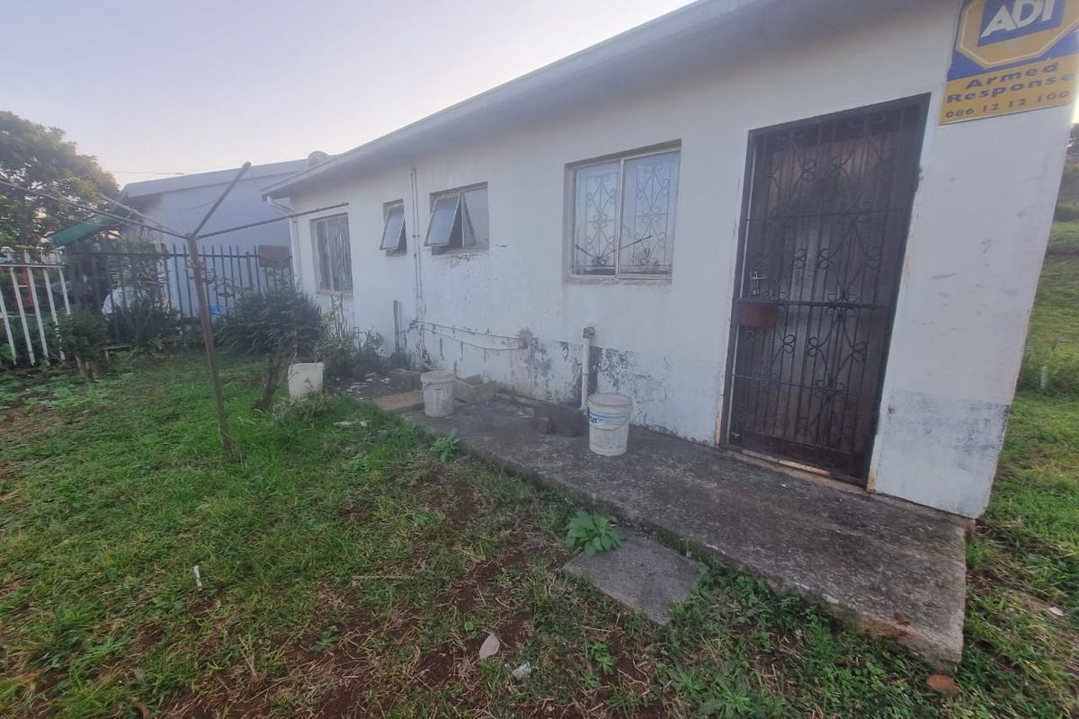 Rear exterior view of the property showing a concrete pathway, security gate, and weathered wall finishes requiring maintenance.