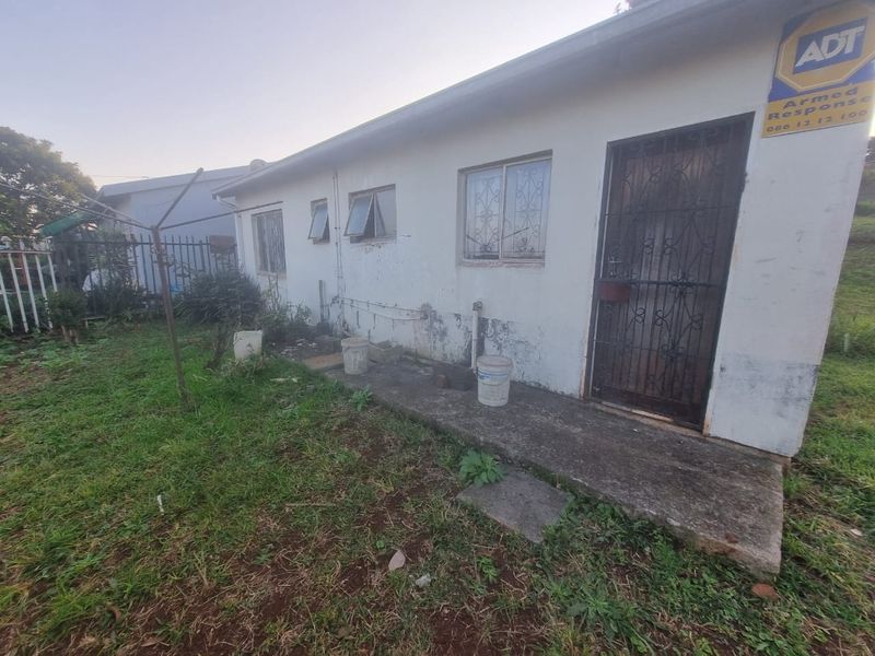 Rear exterior view of the property showing a concrete pathway, security gate, and weathered wall finishes requiring maintenance.