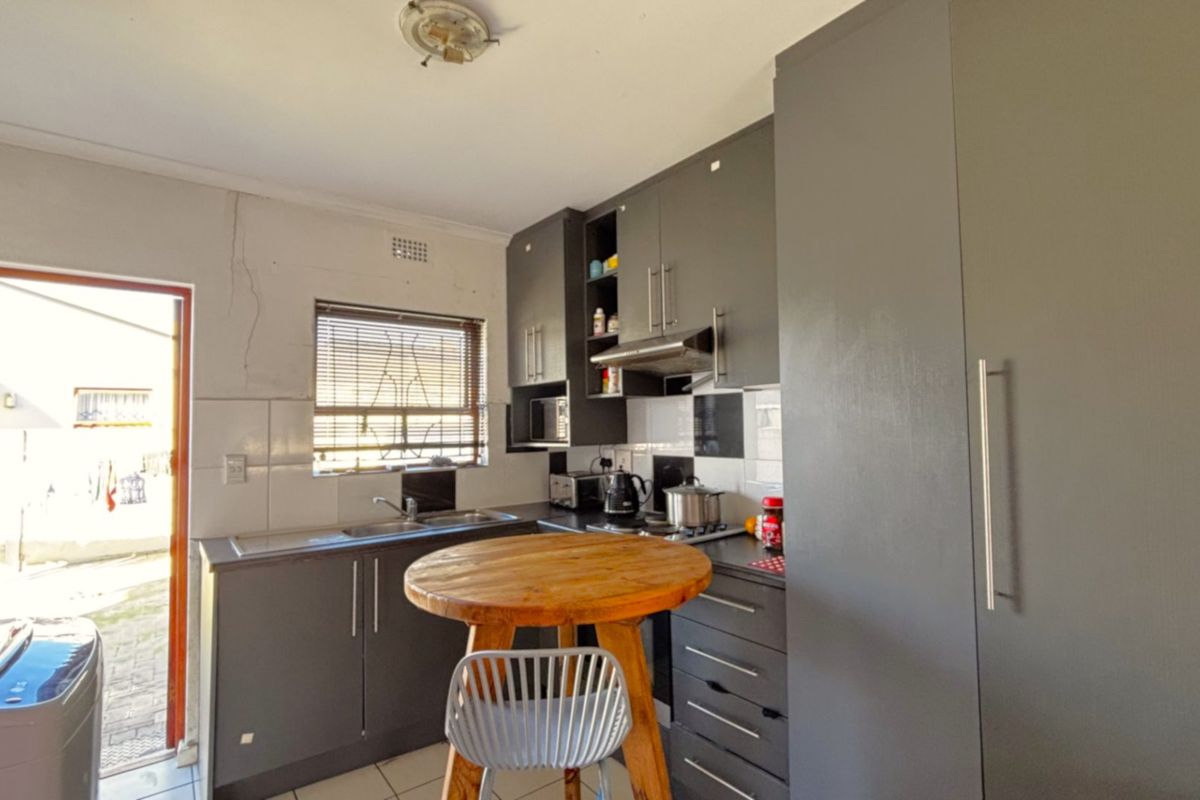 Compact kitchen featuring modern grey cabinetry, tiled backsplash, integrated appliances, and direct access to the exterior.