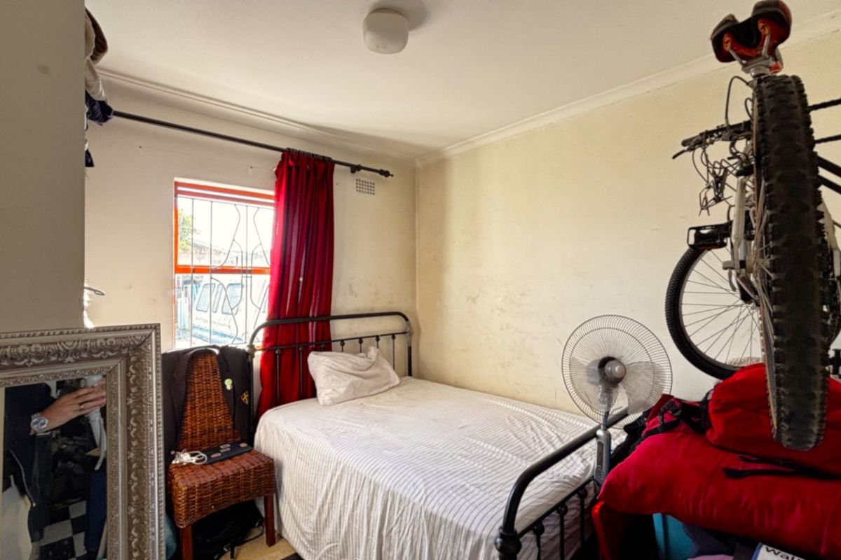 A compact bedroom featuring a window with a security gate and coving detail, requiring cosmetic updates to the wall finishes.