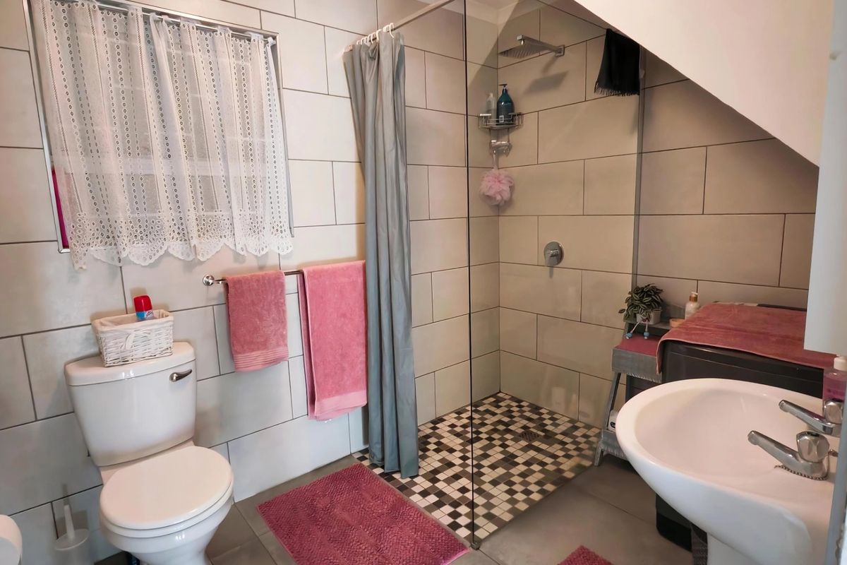 A functional bathroom featuring a walk-in shower with a glass screen, rainfall shower head, pedestal basin, and modern tiled finishes.