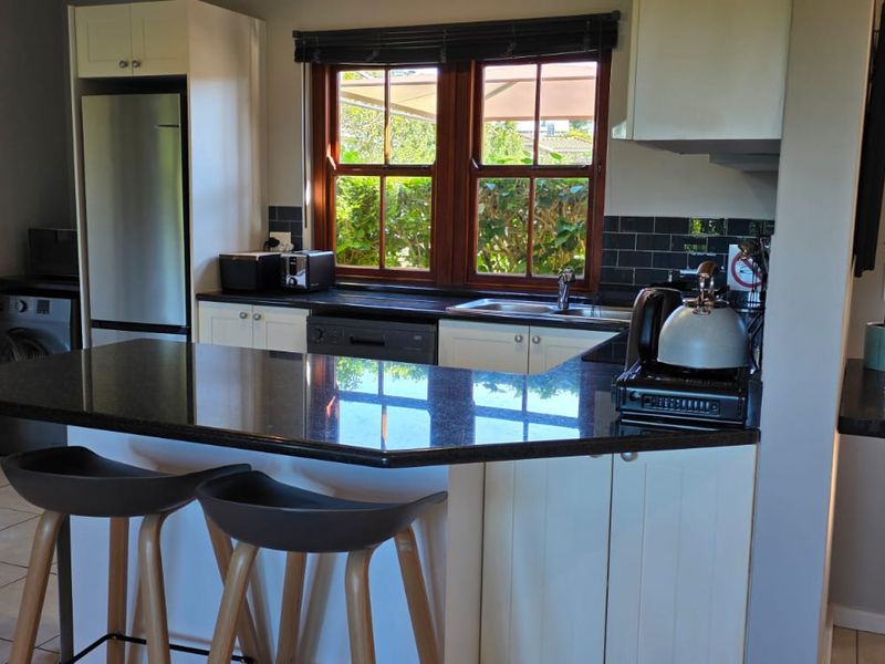 A functional kitchen featuring granite countertops, white cabinetry, a tiled backsplash, and a view through timber-framed windows to the exterior.