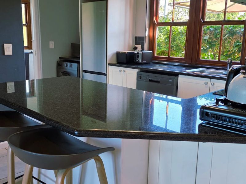 A functional kitchen featuring granite countertops, a breakfast bar, white cabinetry, and a tiled backsplash with views to the exterior.