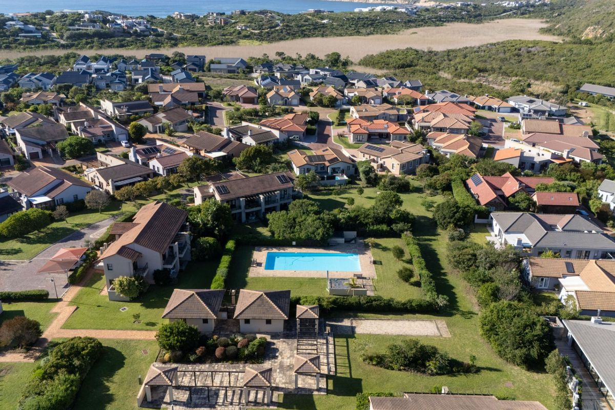 An aerial view of a residential apartment complex featuring a central swimming pool, landscaped gardens, and well-maintained communal outdoor areas.