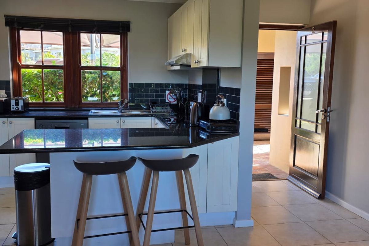 A functional kitchen featuring shaker-style cabinetry, granite countertops, a tiled backsplash, and direct access to an outdoor area.
