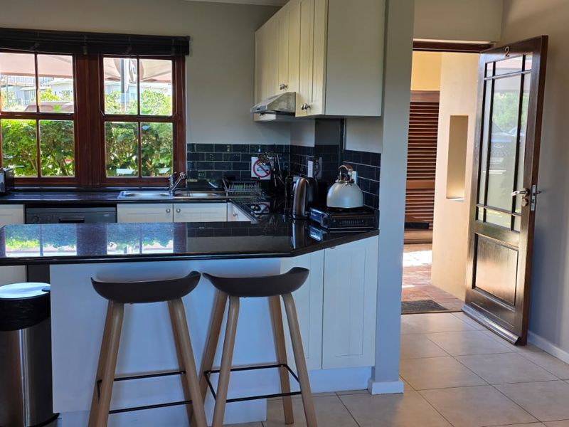 A functional kitchen featuring shaker-style cabinetry, granite countertops, a tiled backsplash, and direct access to an outdoor area.