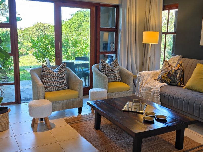 A bright and inviting living room featuring tiled flooring and large sliding glass doors that provide seamless access to the outdoor garden area.