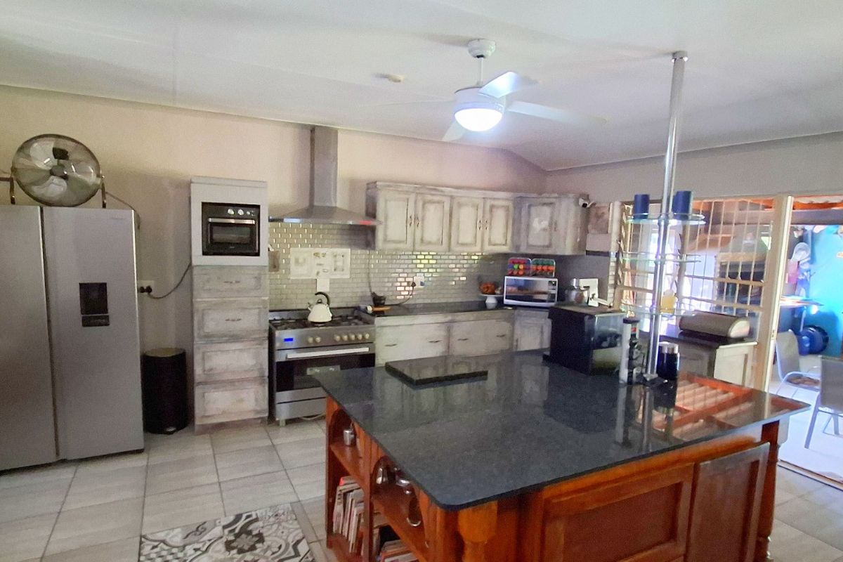 Spacious kitchen featuring a central island with granite countertop, built-in oven, gas hob, extractor fan, and ample cabinetry, opening onto an outdoor patio area.