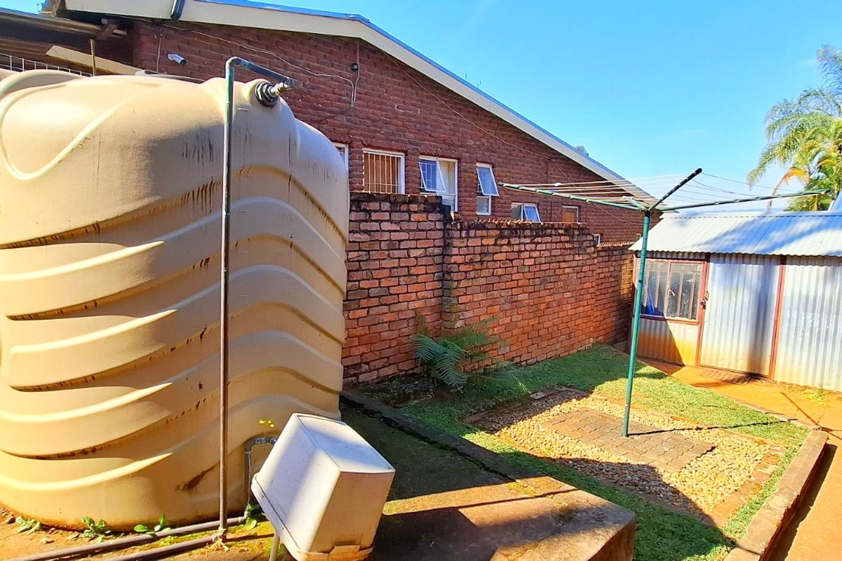 Rear exterior area featuring a large water storage tank, brick boundary walls, a corrugated metal shed, and a paved utility space.