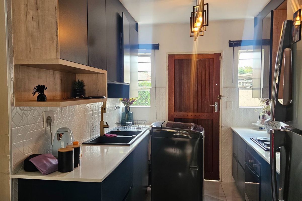 Modern kitchen featuring dark cabinetry, light quartz countertops, brass fixtures, and a tiled backsplash, offering a functional and contemporary cooking space.