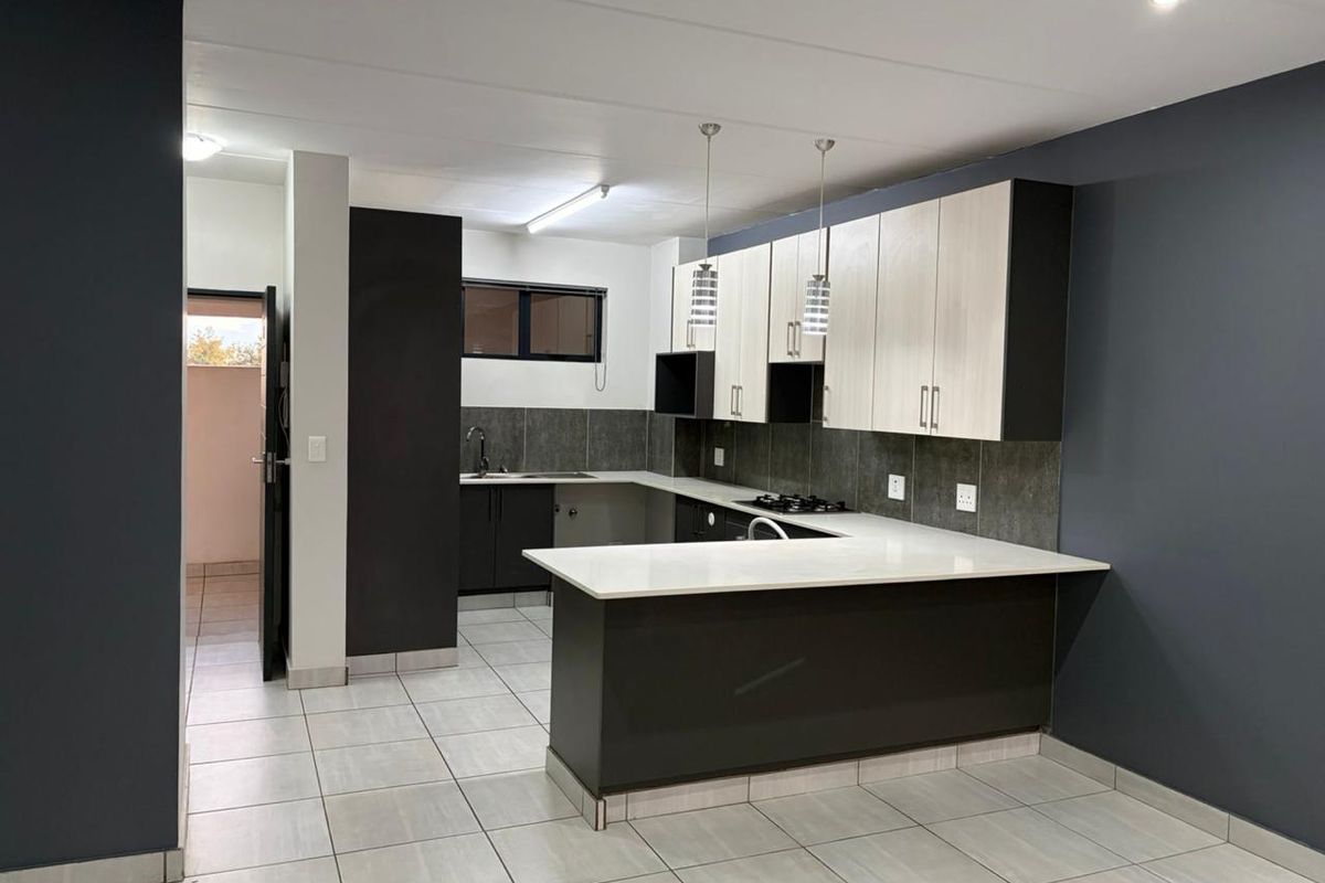 Modern kitchen featuring two-tone cabinetry, stone countertops, a gas hob, and tiled flooring, offering a clean and functional workspace.