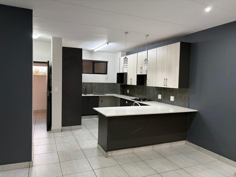 Modern kitchen featuring two-tone cabinetry, stone countertops, a gas hob, and tiled flooring, offering a clean and functional workspace.