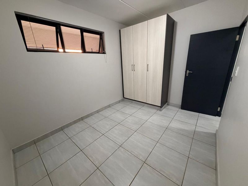 A clean, empty bedroom featuring neutral tiled flooring, a built-in wardrobe, and a window with fitted horizontal blinds.