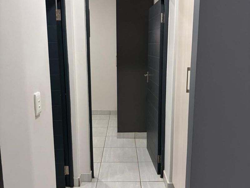 A clean, modern hallway featuring neutral tiled flooring, built-in storage cupboards, and dark-toned internal doors.