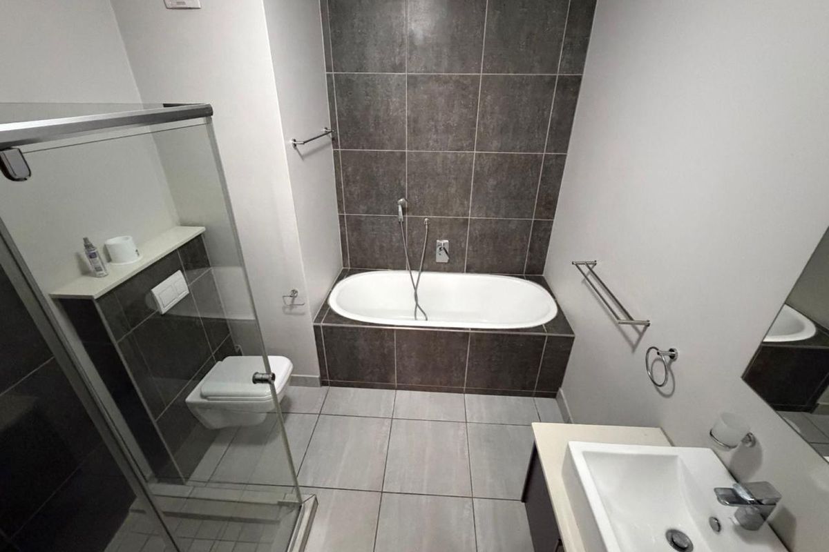 Modern bathroom featuring a built-in bathtub, wall-mounted toilet, glass shower enclosure, and a vanity basin with contemporary tiled finishes.