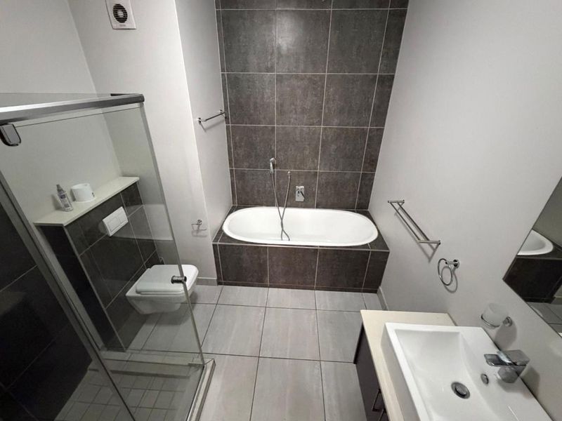 Modern bathroom featuring a built-in bathtub, wall-mounted toilet, glass shower enclosure, and a vanity basin with contemporary tiled finishes.