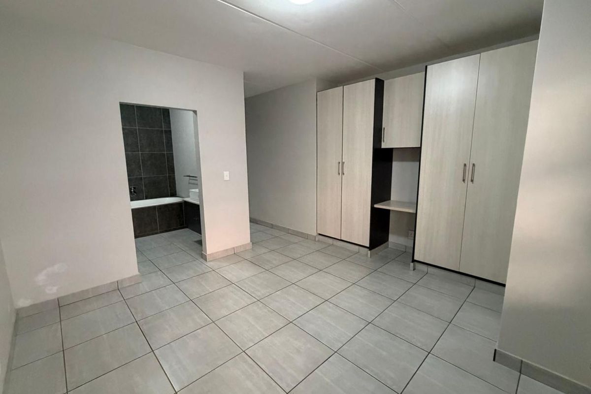 A clean, empty bedroom featuring neutral tiled flooring, ample built-in cupboard storage, and direct access to an en-suite bathroom.