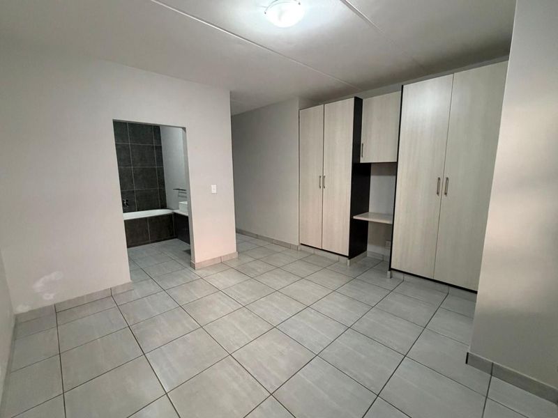 A clean, empty bedroom featuring neutral tiled flooring, ample built-in cupboard storage, and direct access to an en-suite bathroom.