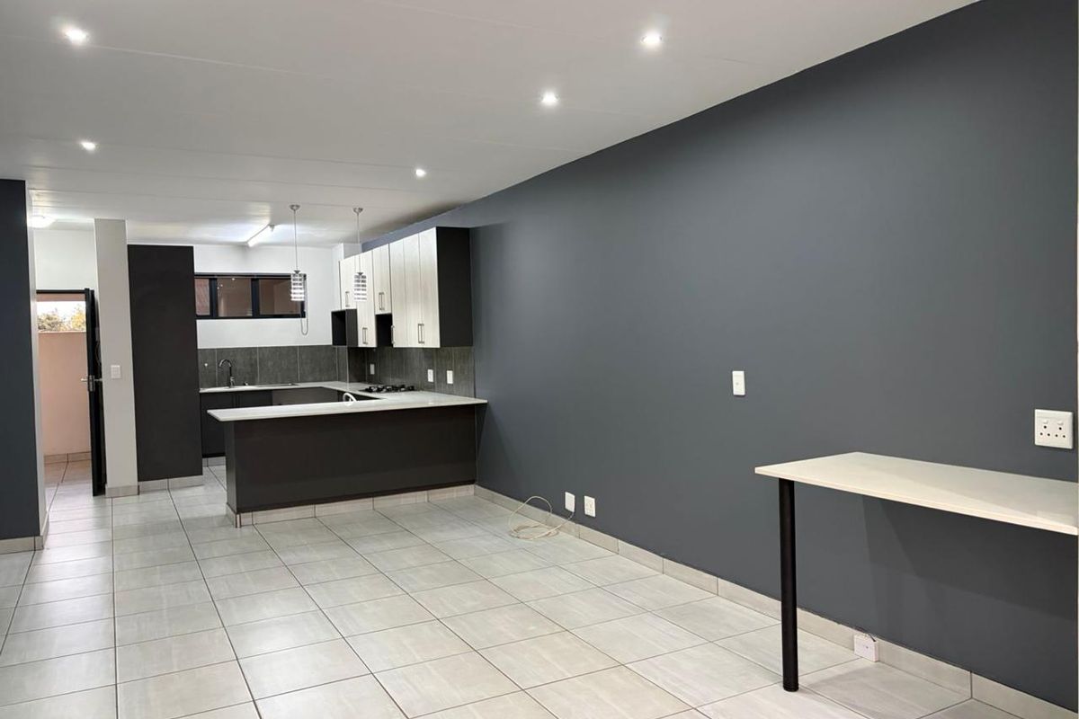 Spacious open-plan kitchen and living area featuring modern two-tone cabinetry, a breakfast bar, tiled flooring, and recessed lighting in a neutral, contemporary setting.
