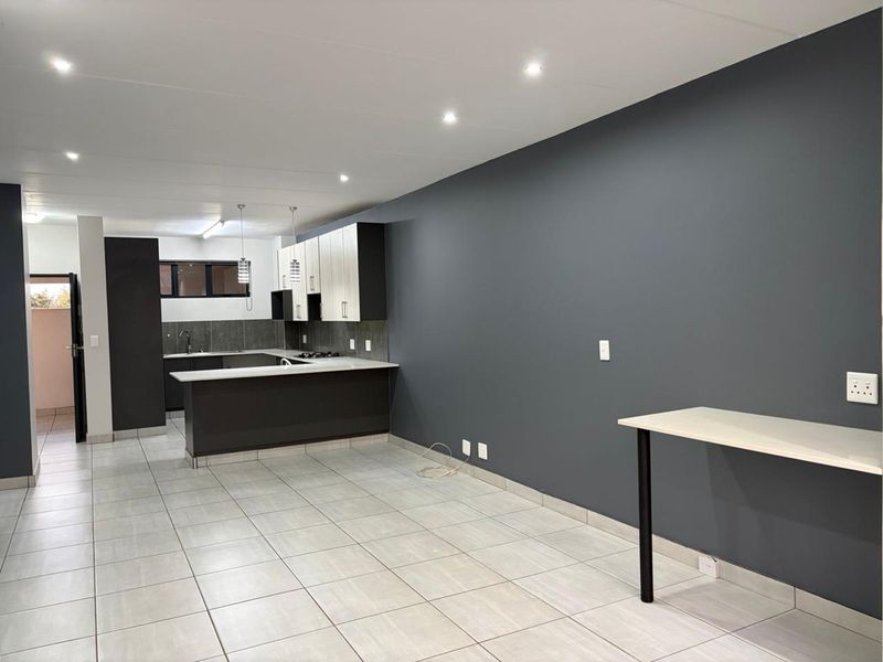 Spacious open-plan kitchen and living area featuring modern two-tone cabinetry, a breakfast bar, tiled flooring, and recessed lighting in a neutral, contemporary setting.