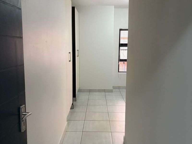 A clean, empty hallway featuring neutral tiled flooring and built-in storage cupboards, leading towards a windowed area.
