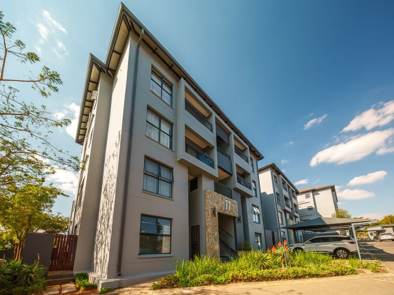 A modern multi-story apartment complex featuring a stone-clad entrance, private balconies, and convenient covered parking facilities within a well-maintained residential estate.