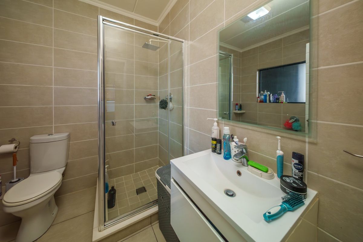 A well-maintained bathroom featuring a glass-enclosed shower, modern vanity basin with mirror, and neutral floor-to-ceiling wall tiling.