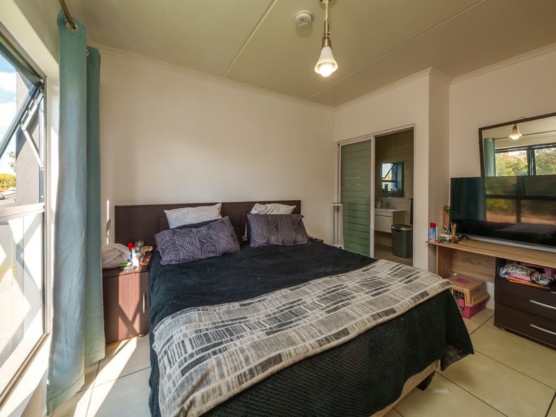A well-lit bedroom featuring tiled flooring, a large window, and an en-suite bathroom access through a sliding door.
