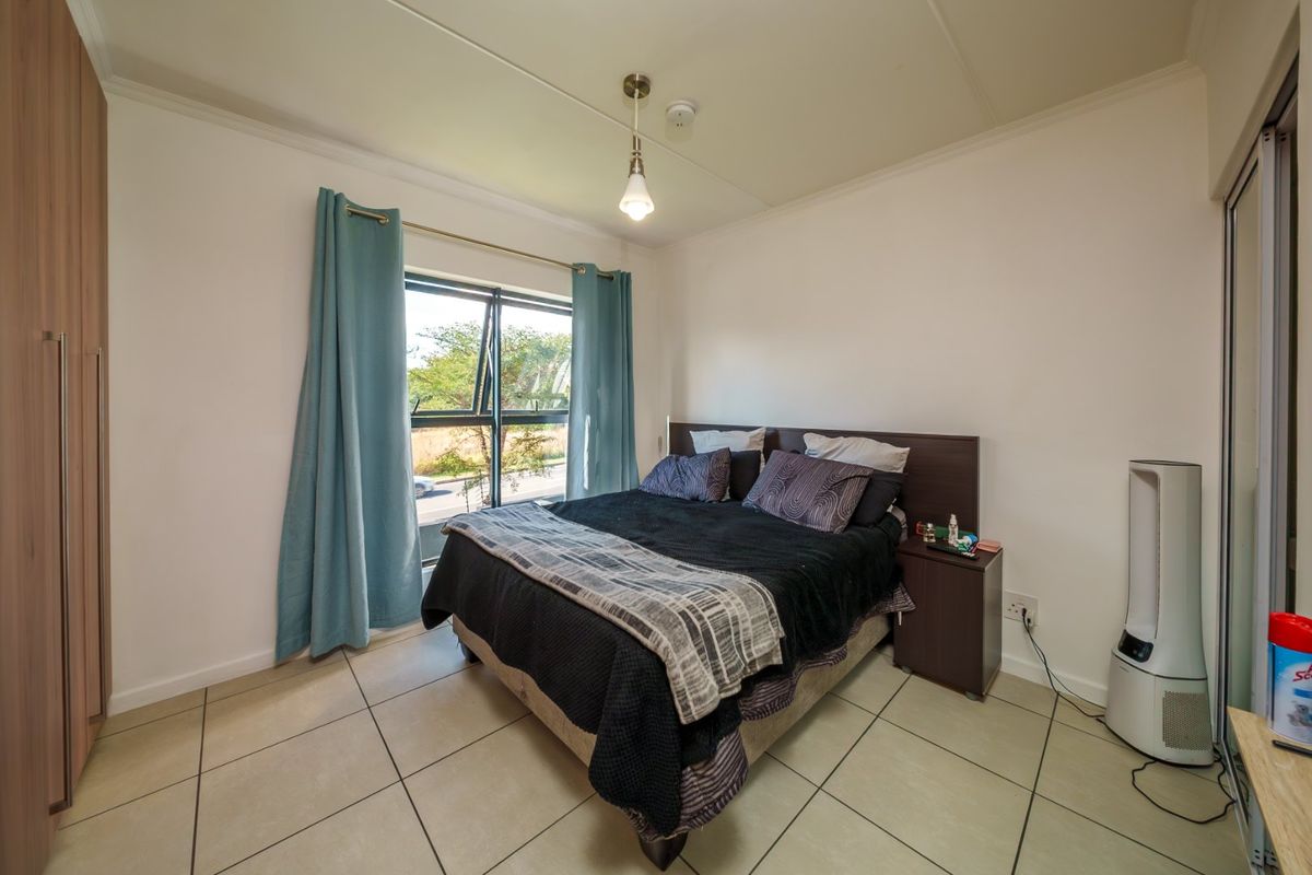 A functional bedroom featuring tiled flooring, a built-in wardrobe, and an aluminium window frame providing natural light.