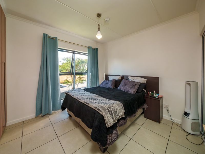 A functional bedroom featuring tiled flooring, a built-in wardrobe, and an aluminium window frame providing natural light.