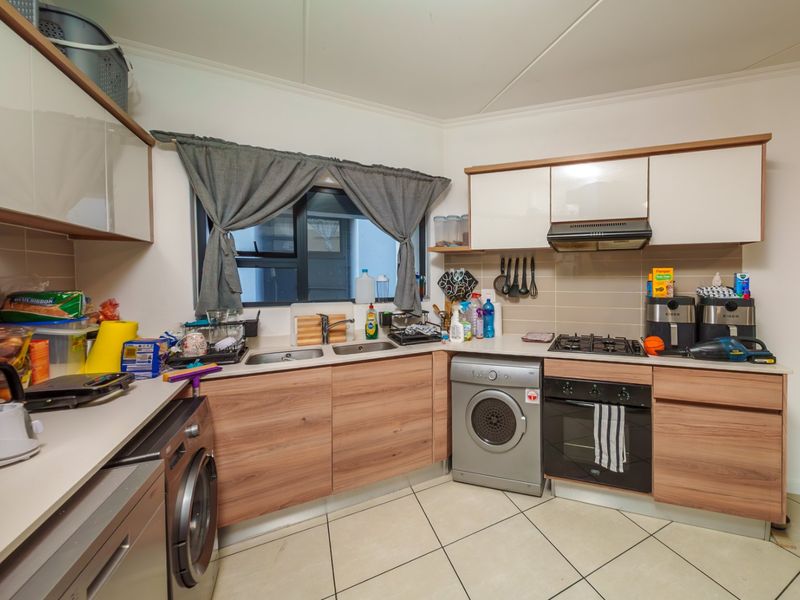 A functional kitchen featuring wood-look cabinetry, light countertops, a gas hob, built-in oven, and tiled flooring with a practical layout.