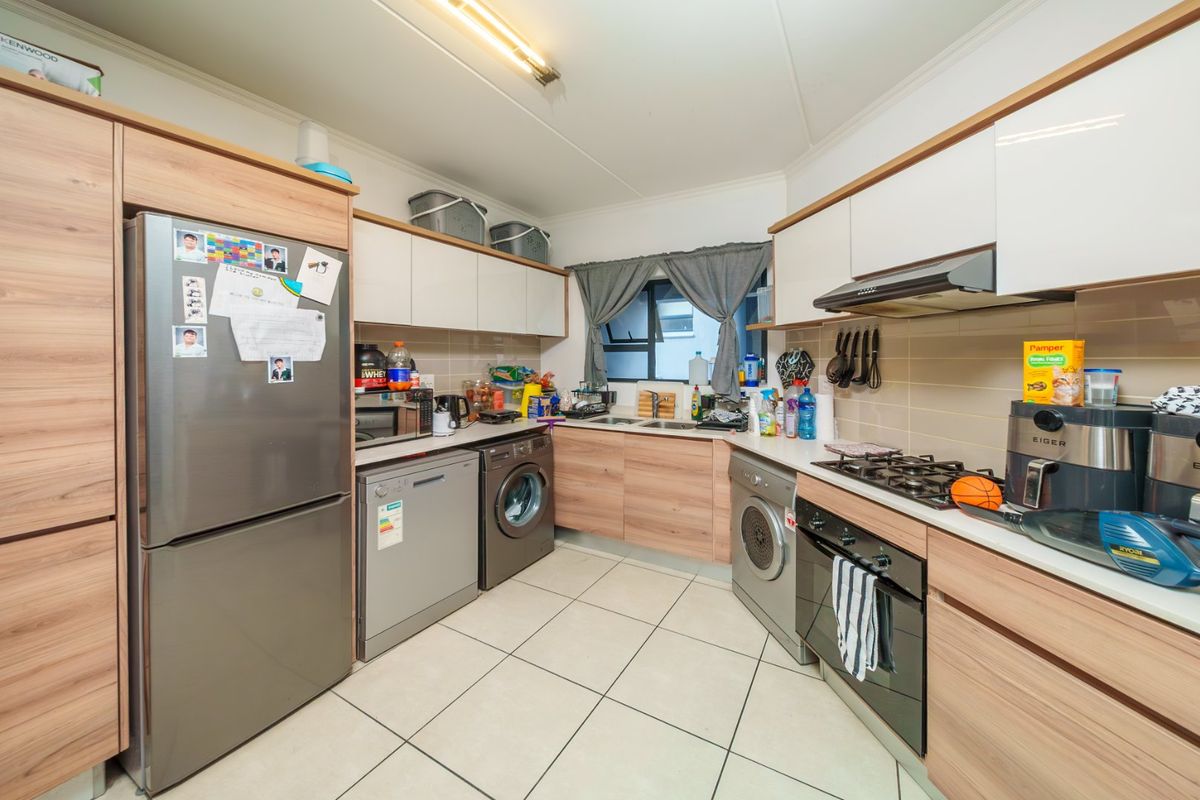 A functional kitchen featuring wood-look cabinetry, a gas hob, built-in oven, extractor fan, and tiled flooring with integrated space for laundry appliances.