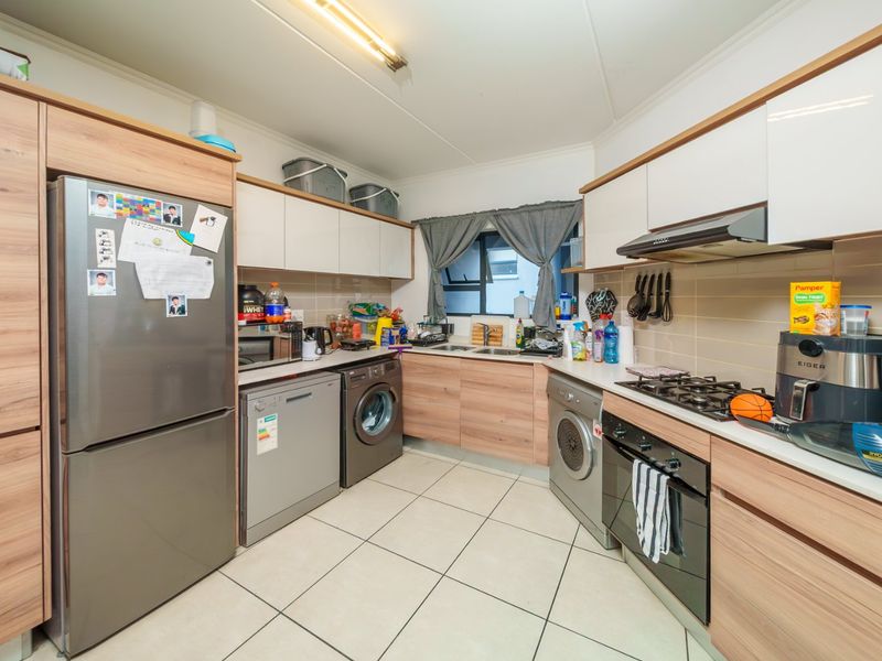 A functional kitchen featuring wood-look cabinetry, a gas hob, built-in oven, extractor fan, and tiled flooring with integrated space for laundry appliances.