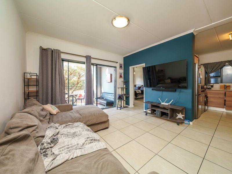 Open plan living area featuring tiled flooring, a feature wall, and sliding glass doors leading to a balcony, with an adjacent kitchen space.