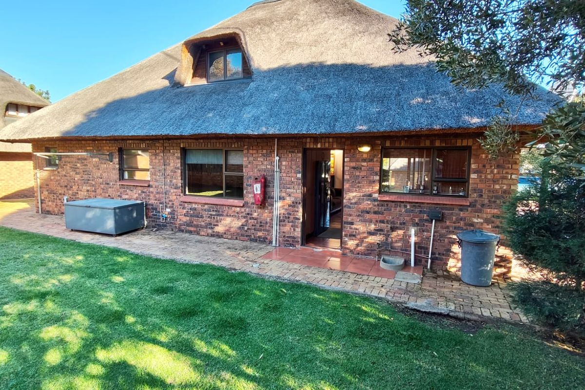 Rear view of a face brick house featuring a traditional thatch roof, paved patio area, and surrounding garden space.