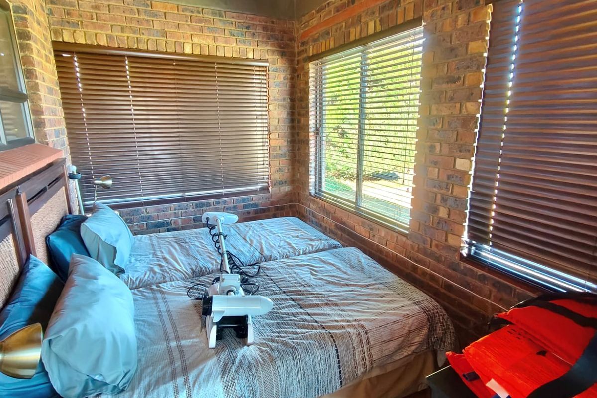 A bedroom featuring exposed brick walls and large windows with venetian blinds, providing natural light and a rustic aesthetic.