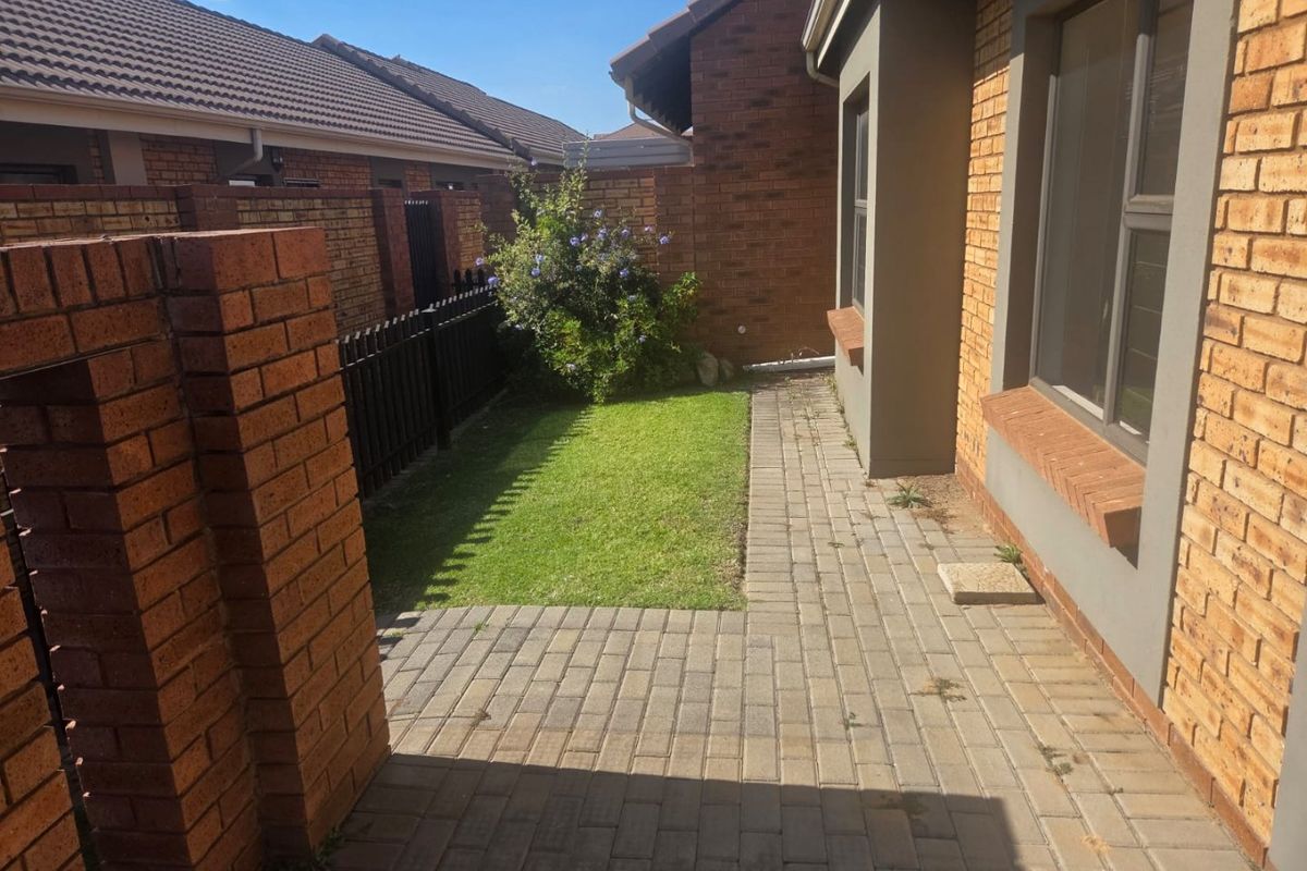 A private rear garden area featuring brick paving, a small lawn, and secure perimeter walling with metal fencing.