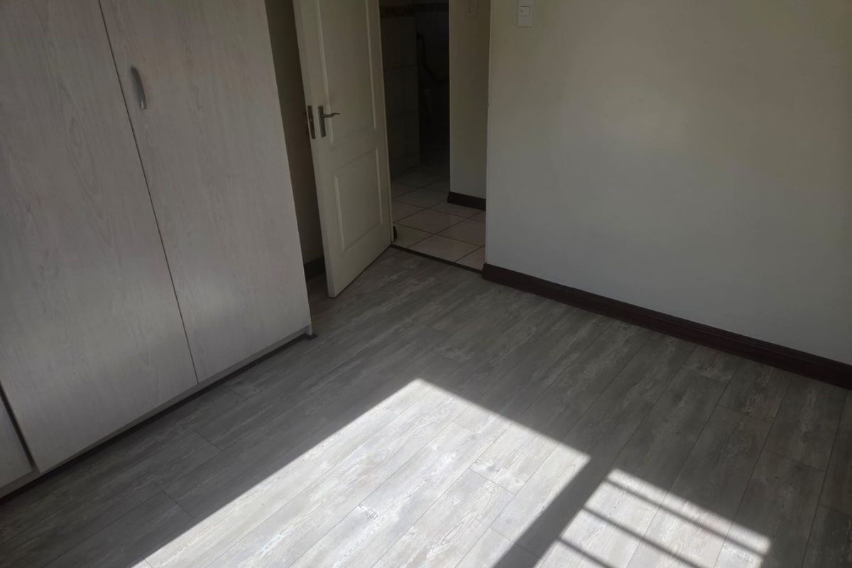 A bright, empty bedroom featuring light-toned laminate flooring, a built-in wardrobe, and direct access to an adjoining bathroom.