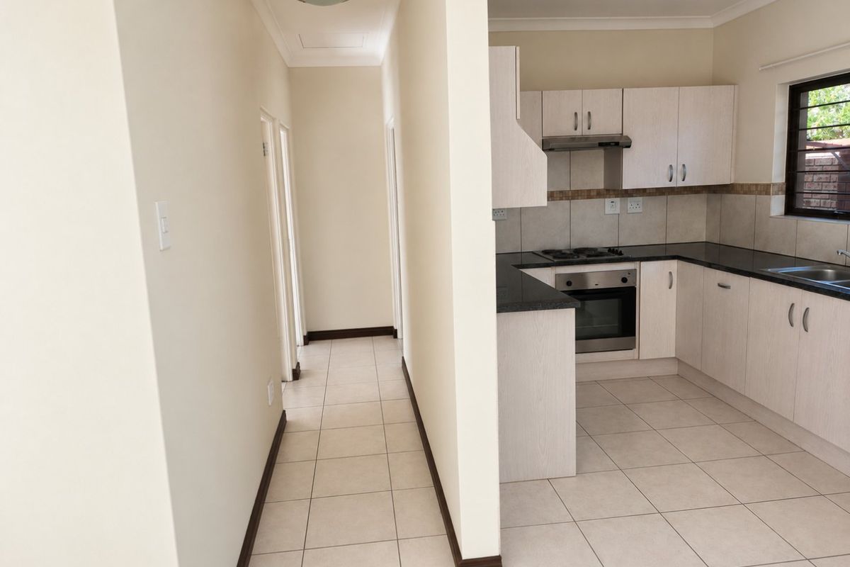 A clean, functional kitchen featuring light-toned cabinetry, granite countertops, built-in oven, gas hob, and tiled flooring, adjacent to a hallway.