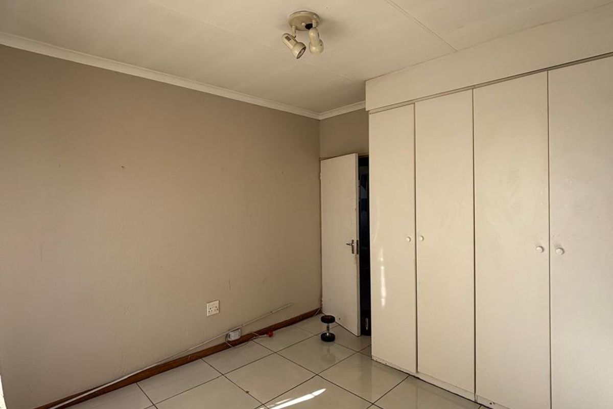 A vacant bedroom featuring neutral tiled flooring and built-in white cupboards, offering a blank canvas for personalization.
