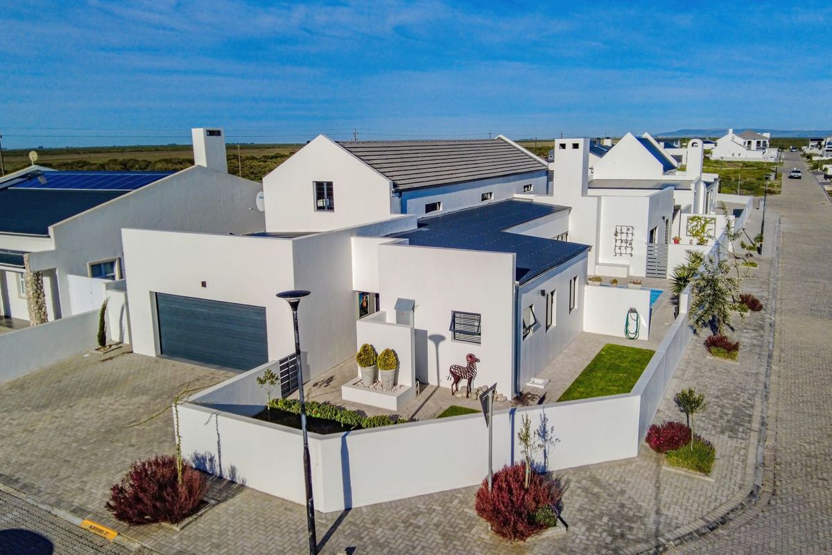 Aerial view of a modern white house featuring a tiled roof, solar panels, a paved driveway, and a secure boundary wall.