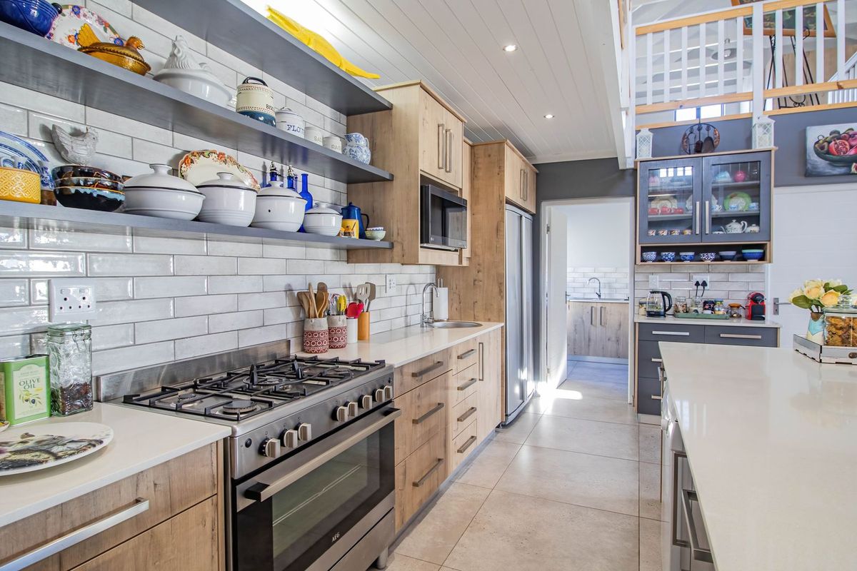 Modern kitchen featuring stone countertops, gas stove, subway tile backsplash, open shelving, and a central island, with a scullery visible in the background.