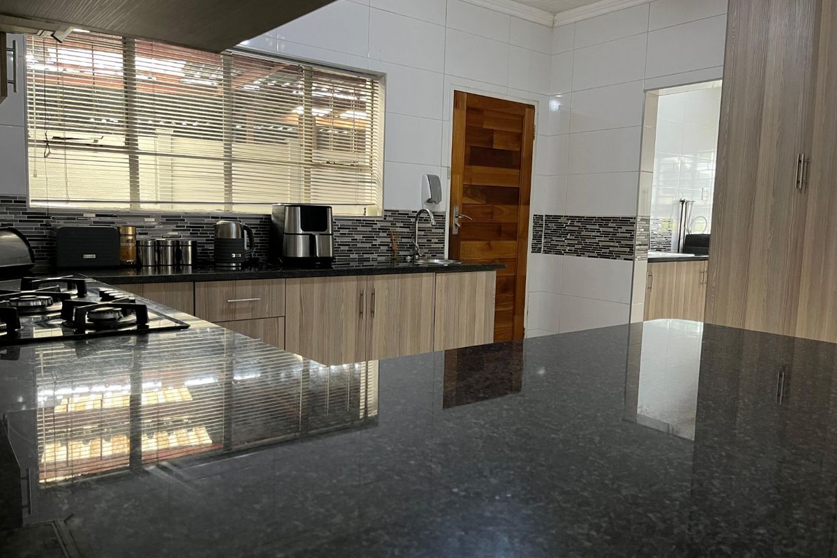 Modern kitchen featuring granite countertops, a gas hob, mosaic tile backsplash, and light wood-grain cabinetry with an adjacent scullery area.