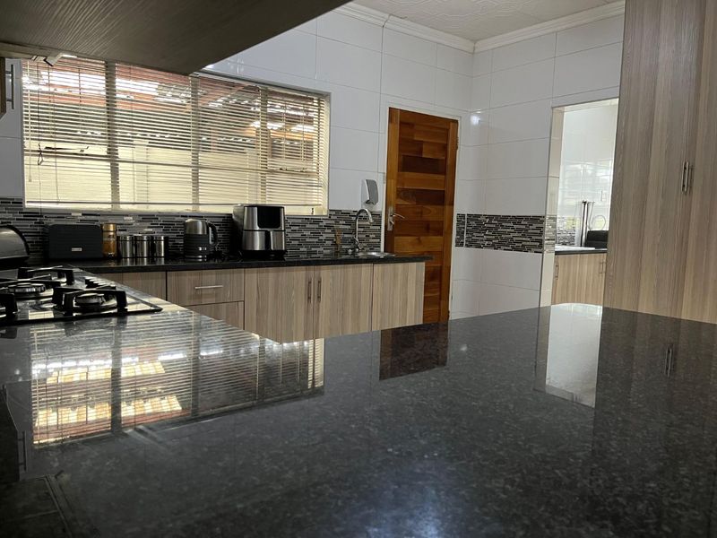 Modern kitchen featuring granite countertops, a gas hob, mosaic tile backsplash, and light wood-grain cabinetry with an adjacent scullery area.