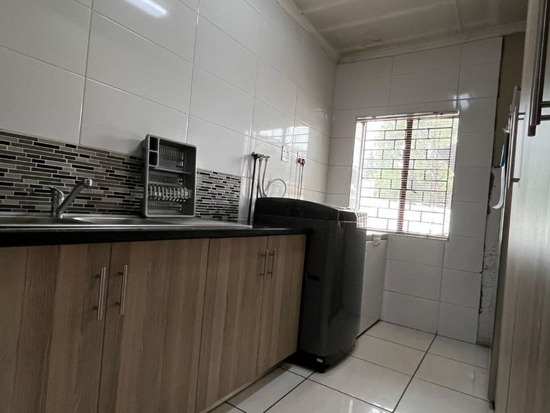 Functional laundry area featuring built-in cabinetry, tiled splashback, and tiled flooring, providing a practical space for household utility tasks.