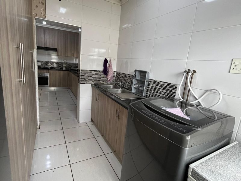 Functional laundry area featuring built-in cabinetry, tiled splashback, and plumbing connections, with direct access to the adjacent kitchen space.