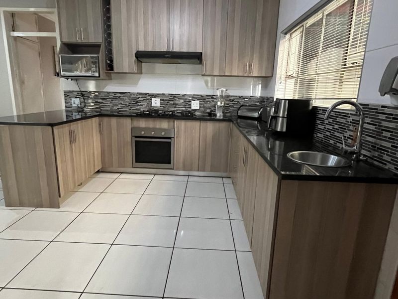 Modern kitchen featuring wood-finish cabinetry, granite countertops, built-in oven with gas hob, and a decorative tiled ceiling.