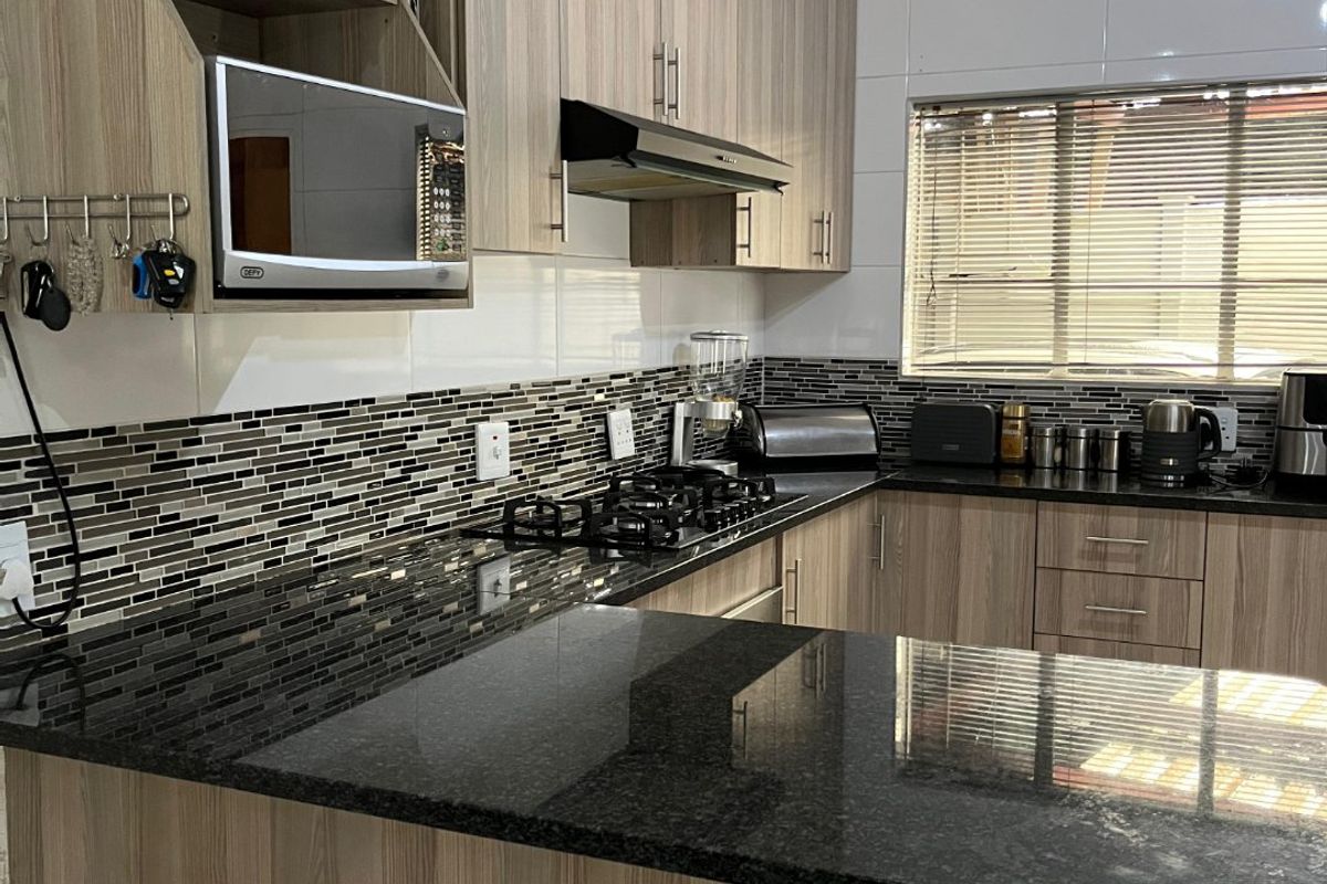 Modern kitchen featuring wood-grain cabinetry, granite countertops, a gas hob with extractor, and a decorative ceiling finish.