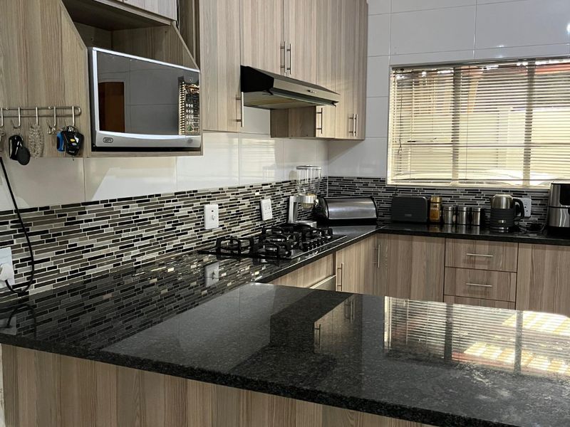 Modern kitchen featuring wood-grain cabinetry, granite countertops, a gas hob with extractor, and a decorative ceiling finish.