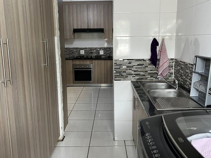 A functional scullery area featuring built-in cabinetry, double sink, and tiled finishes, leading through to a modern kitchen with built-in oven and hob.
